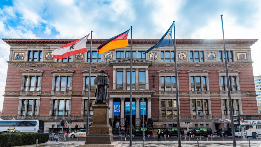 Fasaden til Gopius-Bau-bygget i bakgrunnen. Tre flagg vaier i vinden på plassen foran bygget. Foto.