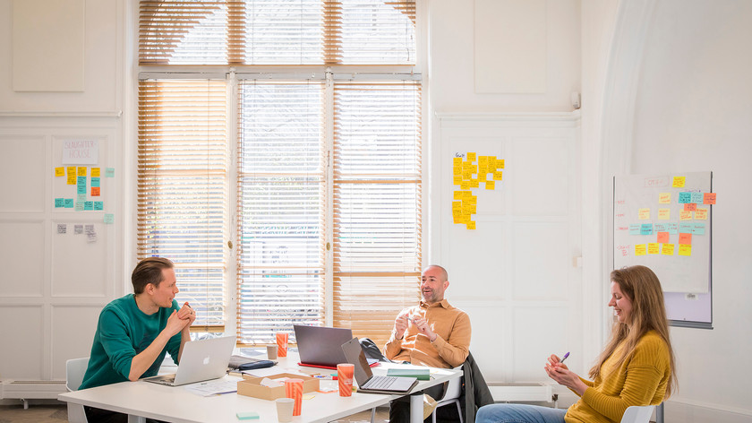 Foto. Tre personer rundt et bord i et rom med et stort vindu.