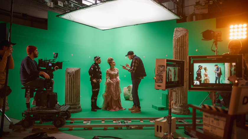 Filmstudio med grønnskjerm. En fotograf sitter bak kamera. En regissør gir instruksjoner til to skuespillere. Foto.
