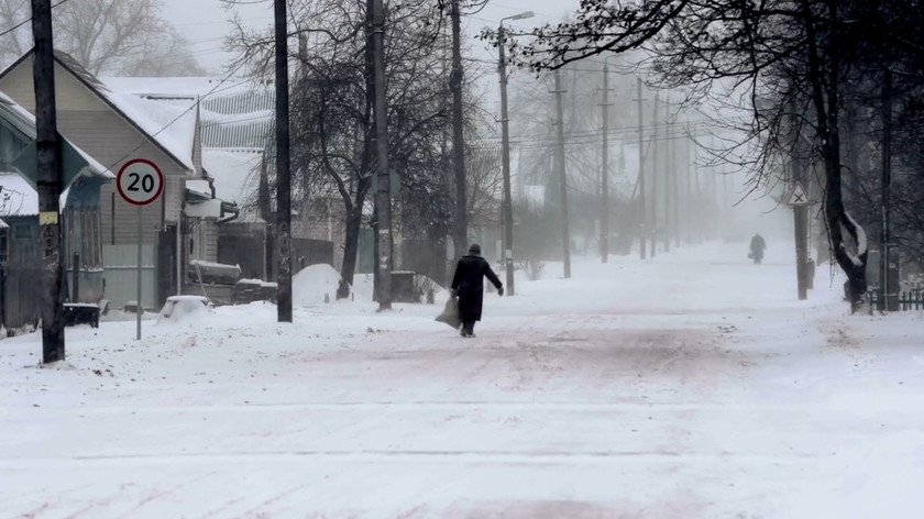 To personer går langs en snødekt vei. Langs veien er det gatelys, trær og hus. Foto.