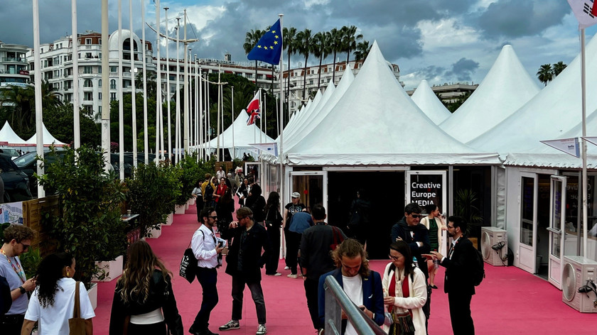 Foto. Teltlandsby langs en rosa løper. Det er mange mennesker utenfor teltene. Palmer og bygg i bakgrunnen.